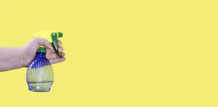 Sprayer for flowers isolated on a yellow background, in a female hand. Bottle for flower care. Water spray.の写真素材