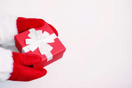 Santa in red gloves gives a gift. Red box with a bow in the hands of Santa Claus, isolated on a...