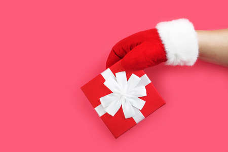 Santa in red gloves is holding a gift. Red box with a bow in the hand of Santa Claus, isolated on a...