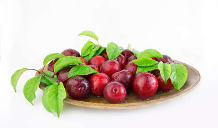 Fresh plums with leaves on a wooden plate close-up. Copy space