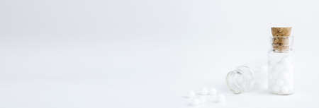 Homeopathic globules and glass bottle on white background. Alternative Homeopathy medicine herbs, healtcare and pills. Banner. Copy space.の写真素材