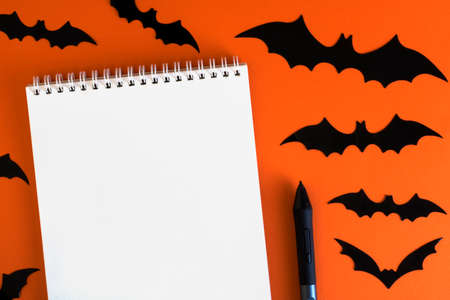 Blank notepad on orange background with paper bats silhouettes, traditional Halloween decor. The...