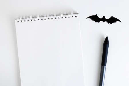 Blank notepad on white background with next to the black pen, and paper bat silhouette, traditional...