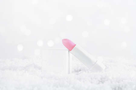 A white tube of pink lipstick balm to protect and nourish lips. Winter season cosmetics. Mock up container in the snow. Christmas present for women idea. Copy spaceの写真素材