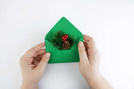 Green envelope with a Christmas branch in female hands on a white background. Christmas mail or...
