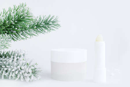 Jar of cream and lip balm on a white background with a Christmas branch. Container for body care...