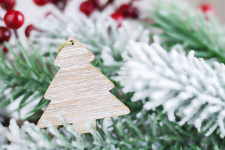 Wooden pendant on a Christmas tree. Christmas decorations for the fir on the background of a blurred fir with snow. Postcard for Christmas or New Year. Copy spaceの写真素材