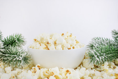Popcorn in a white bowl next to spruce branches, on a white background. Selective focus. Christmas or New Year concept. Corn snacks.の写真素材
