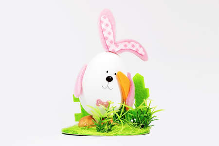 Easter egg with ears in the form of an Easter bunny, with carrots on a green lawn. Easter card. Minimal easter conceptの写真素材