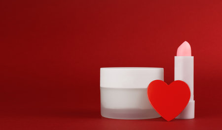 Jar of cream and lip balm on a red background with heart. Container for body care balm. Concept background for Valentine's Day. Blank advertisement with copy spaceの写真素材