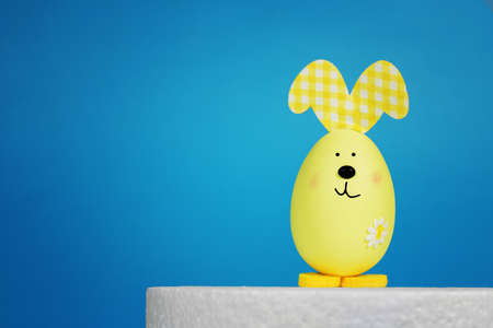 Yellow Easter bunny in the form of an egg on a blue background. Easter background concept, for text.の写真素材