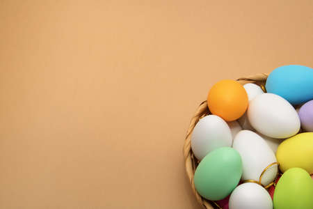 Beige background with green, pink, white, lilac, yellow and beige Easter eggs in a basket. Colorful...