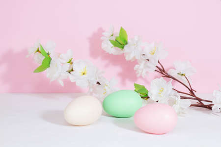 Easter eggs, pink, beige and green, on a concrete white table, next to flowers on a pink background.の写真素材