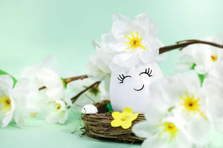 A happy or cute decorated Easter egg in a basket, with flowers on greenの写真素材