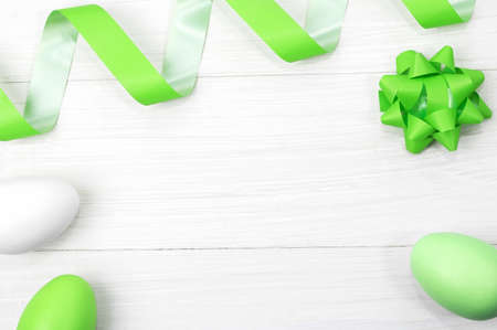 Green and white Easter eggs with green festive ribbon and bow on a white gray wooden background. Easter concept. Top view. Flat lay. Copy spaceの写真素材