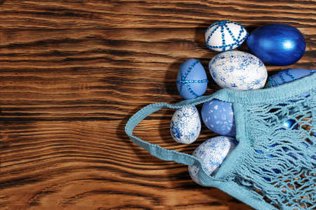 Blue, white, with rhinestones Easter eggs in a string bag on a trendy yellow wooden background. The minimal concept of Easter. Top view. Easter card with a copy space for text.の写真素材