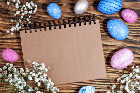 Craft notebook for text on trendy wooden eco background with pink and blue Easter eggs and white flowers. Top View. Copy spaceの写真素材