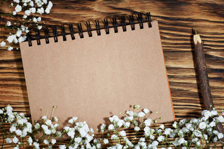 Eco sheet of recycled notepad and wood pen on natural wood eco-friendly background with white flowers. Layout for an advertising post. Top view. Copy spaceの写真素材