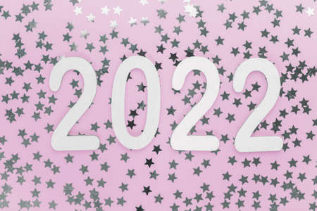 Happy new year wooden numbers 2022 on a festive pink background with sparkles, stars. Greetings,...
