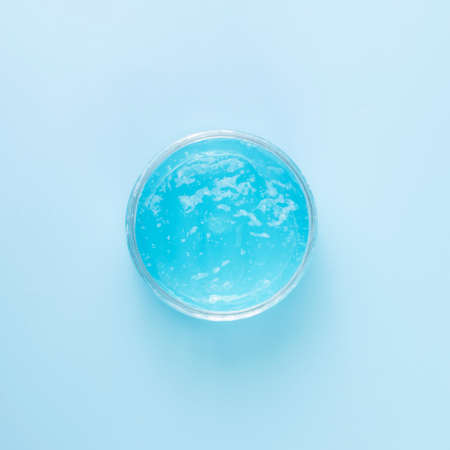 Liquid transparent gel for cleansing the face in a transparent jar on a blue background....