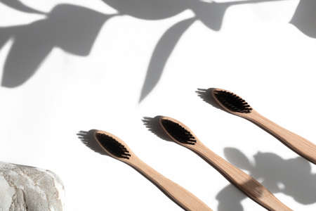 Bamboo toothbrushes isolated on white concrete background with plant shadows. The concept of...