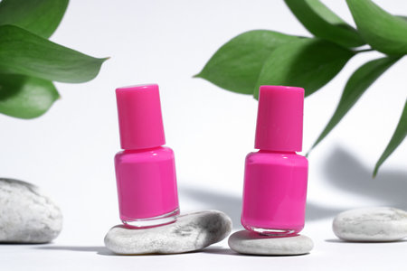 Manicure or pedicure background. Creative mockup of isolated cosmetics bottles with pink nail polish with plant, on stone, on white background with hard shadows from plants. Concept of nail care.の写真素材
