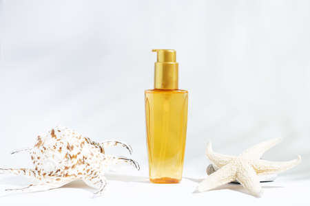 Clear bottle of yellow-orange oil for sun, tanning or hair protection. White background with cosmetic oil and seashells. Summer care cosmetics.の写真素材