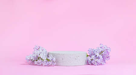 Concrete cylindrical podium with lilac flowers on a pink background with hard shadows. Minimal empty cosmetic product presentation scene. Geometric podium.の写真素材
