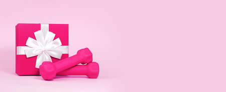 Pink dumbbells near gift box with bow isolated on pink background. Concept of discount, gift or surprise for fitness, home workout, activity and sport, healthy lifestyle. Women Health. Bannerの写真素材