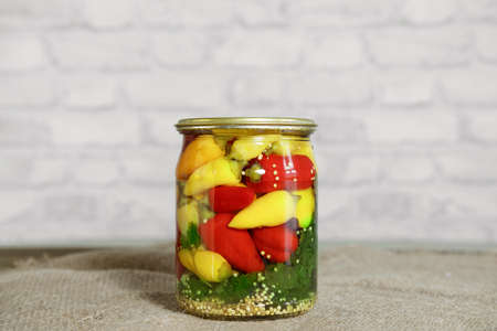 Mini chili peppers of red, yellow and orange colors, canned in glass jars with herbs, on a wooden table. Homemade pickled peppers in Asian style. Preparations for the winter. Copy spaceの写真素材