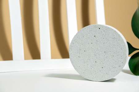 A podium made of concrete with green leaves, for the presentation of packaging and cosmetics, on a white beige background with hard shadows. Product display with white concrete texture, stone texture.の写真素材