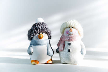 Happy snowman and penguin in a hat and scarf on a white background with hard shadows. Concept christmas and new year background. Christmas Minimalism.の写真素材