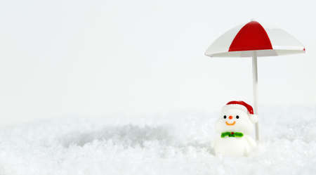 Layout of winter beach christmas holiday holiday. Happy snowman on a snowy white background under a beach umbrella. New Year and Christmas tourism and recreation. Banner.の写真素材