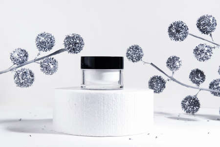 Christmas cosmetic white background. Mockup of moisturizer cosmetic product in a jar on a cylinder podium on a white background with Christmas decorations. Cosmetology or winter skin care concept. Christmas gifts for women. Copy spaceの写真素材