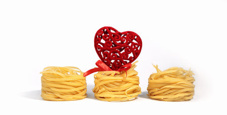 Food for Valentine's Day. Italian pasta. Spaghetti Capellini, with a creative red heart with a bow, isolated on a white gray background, with hard shadows. Pasta in the form of nests on Valentine's Day. Creative photo of pasta.の写真素材
