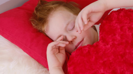 Morning in bed children. A cute funny cheerful boy wakes up in the morning and lies in bed, stretches, rubs his eyes with his hands and smiles. video clip 4k. Relaxation in bed.の写真素材