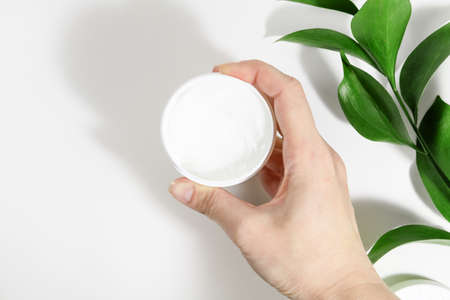 A woman's hand holds a mock-up of a cosmetic tube with a cosmetic cream on a white background with...