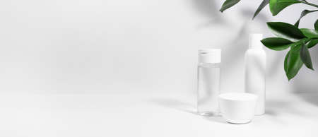 White cosmetics background. Cosmetic bottle containers with green plant leaves. Blank label package for branding mock-up, with hard shadows. Natural organic beauty product concept. Bannerの写真素材