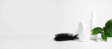White cosmetics background with shadows. Containers for cosmetic bottles for hair care and comb, with green plant leaves. Empty label pack for branding mockup with hard shadows. The concept of natural organic cosmetic products for hair. Bannerの写真素材