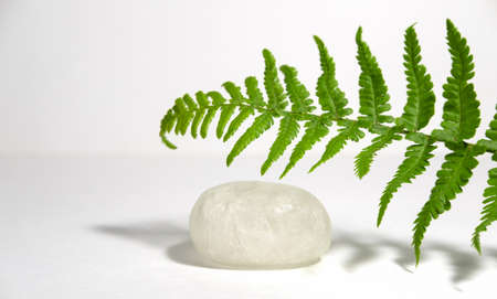 White transparent crystalline alum or potassium alum isolated on white background with tropical leaves and hard shadows. Eco item for body care or water treatment. Spa treatments and skin care, neutralization of bacteria and sweat odor.の写真素材