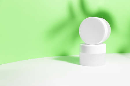 Mockup of a white jar of cream on a white-green geometric gray background, on a white table with hard shadows and tropical leaves shadow. Stylish product appearance, personality.の写真素材
