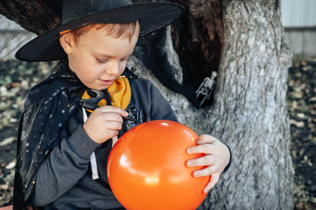Halloween kids. Cute little boy, child in a witch hat draws on an orange Jack O Lantern balloon. Happy Halloween.の写真素材