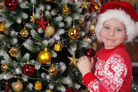 Christmas dreams of a child. Merry Christmas kids. A boy in a Santa hat, near a Christmas tree with...