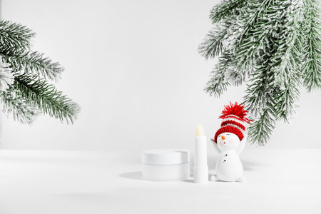 White jar of skin care cosmetics on a white surface with a snowman. winter cosmetics. Empty container with fir branches background. Christmas gift ideas for women.の写真素材