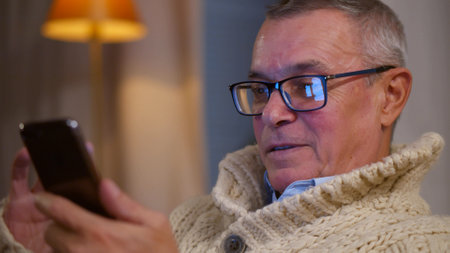 Close up of retired man relaxing at home and surfing internet on smartphoneの写真素材
