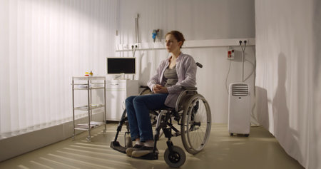 Depressed young woman patient in hospital sitting in wheelchair while doctors passing by.の写真素材