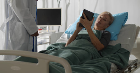 Senior female patient lying in hospital bed and signing online document on digital tabletの写真素材