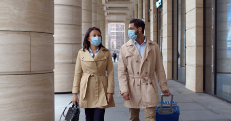 Business colleagues in safety mask walk outdoors with luggageの写真素材