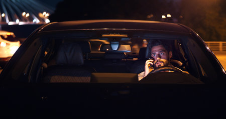 Angry man sitting in car and arguing on smartphone late in eveningの写真素材