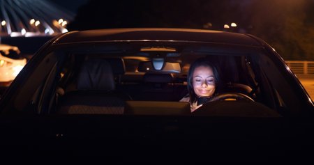 Young woman texting on smartphone sitting in car at parking lotの写真素材